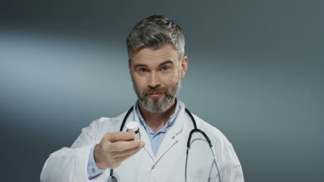 Portrait-shot-of-the-Caucasian-man-doctor-shaking-pills-in-bottle-and-the-doing-gesture-like-offering-it-to-the-viewer-in-camera.-Close-up.